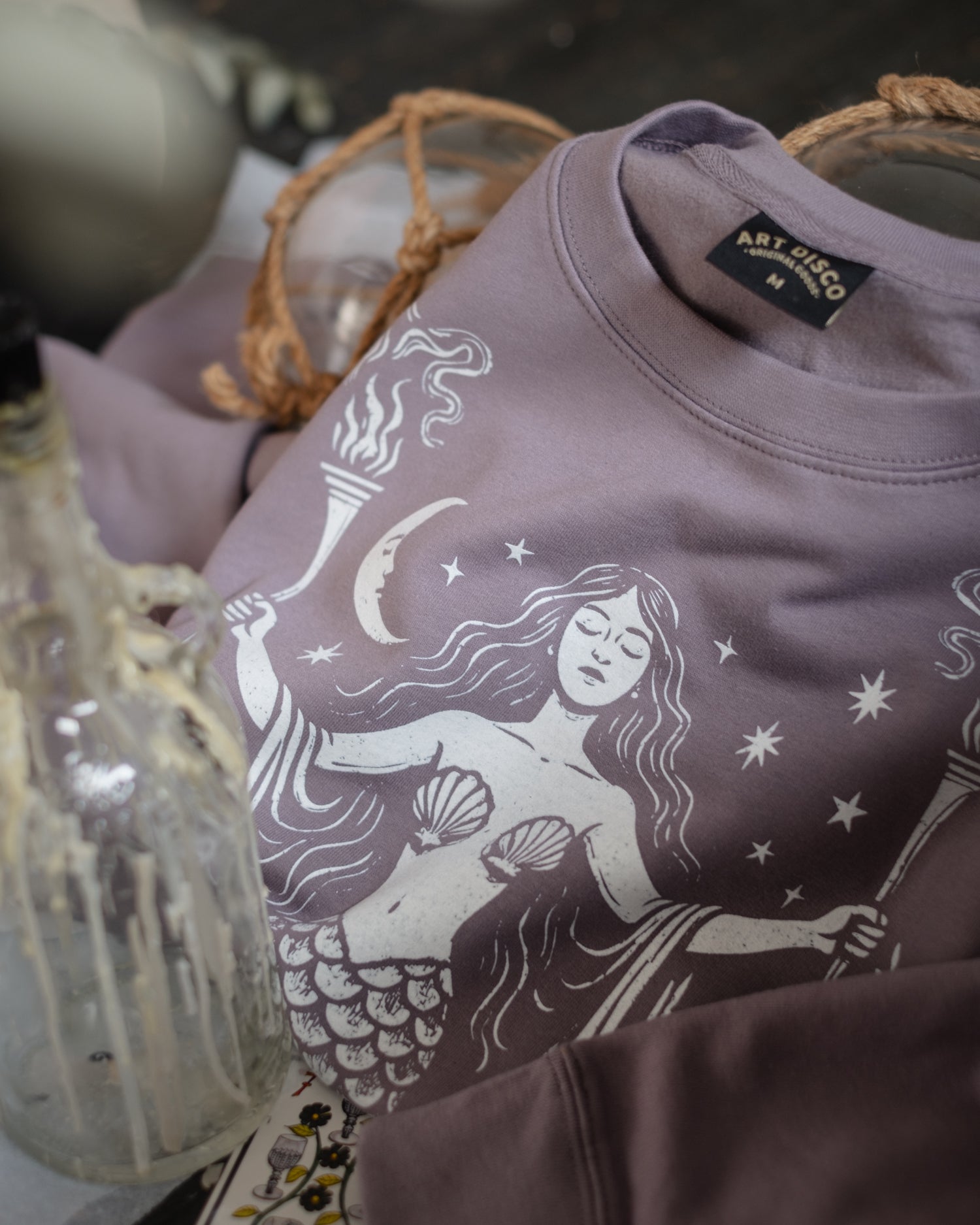 Purple hoodie with mermaid design and 'Art Disco' label on a dark background